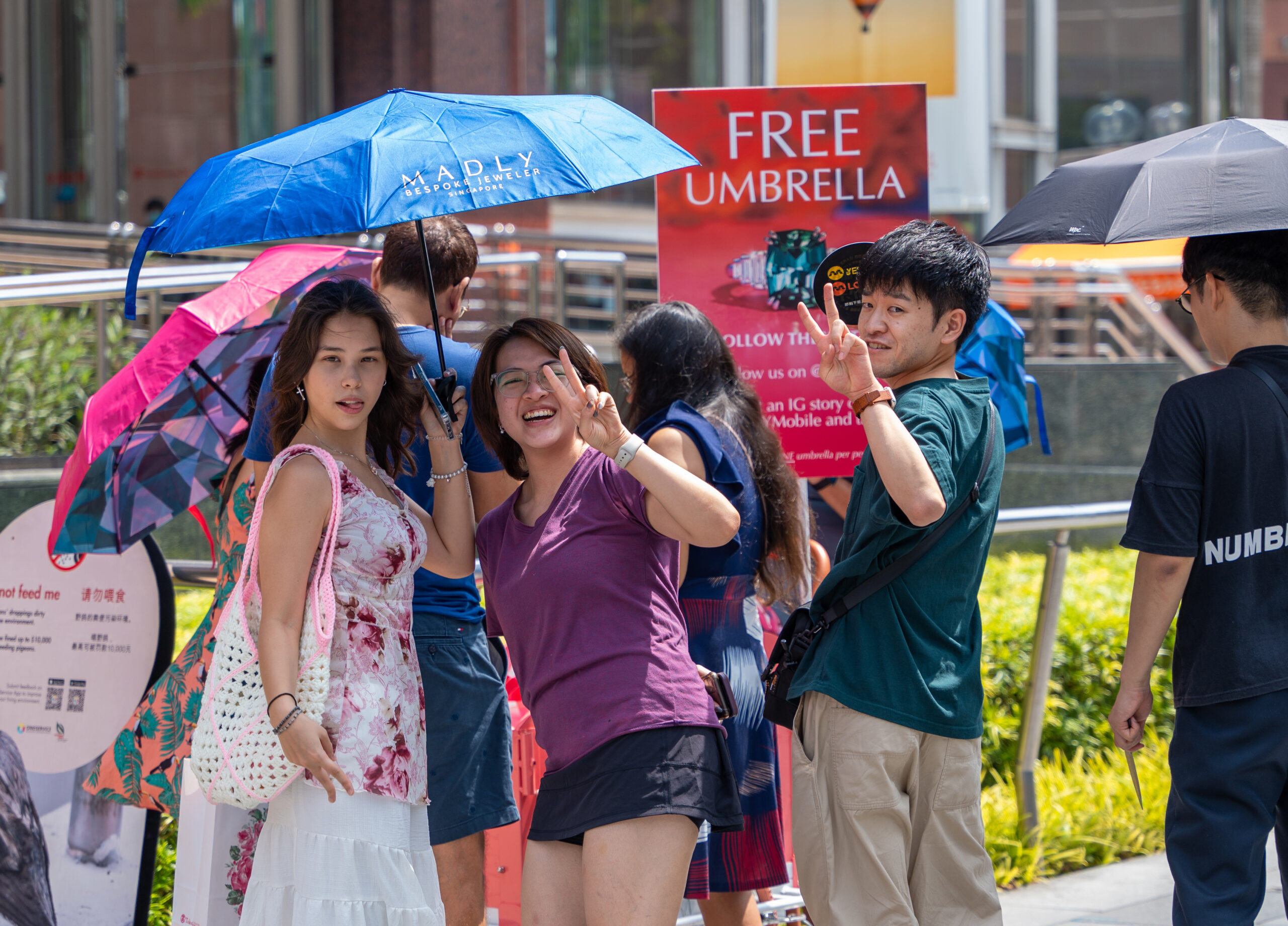 Eurasian and Asian girl under a blue umbrella, next to a Japanese man, making the peace sign with a bicycle cart in the background along Orchard Road