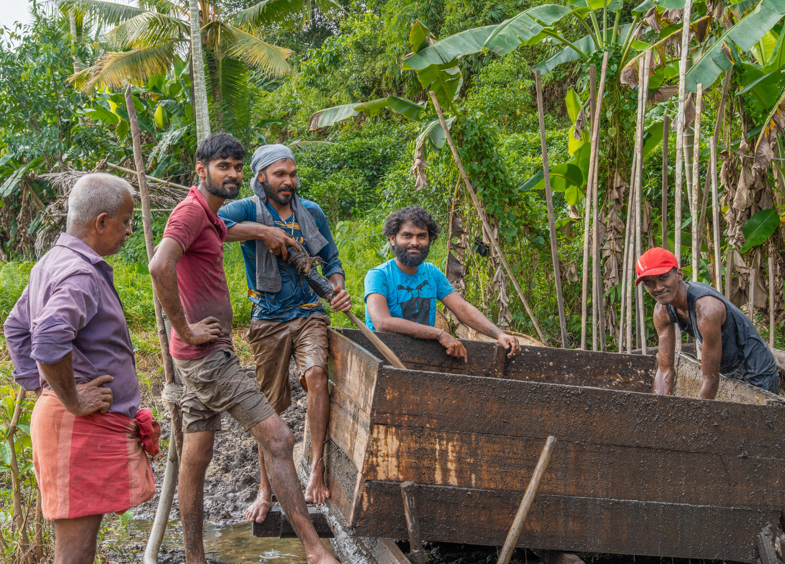 Group of Sri Lankan men smiling and crowding around a gem washing slough and machinery in a mining area in Sri Lanka.