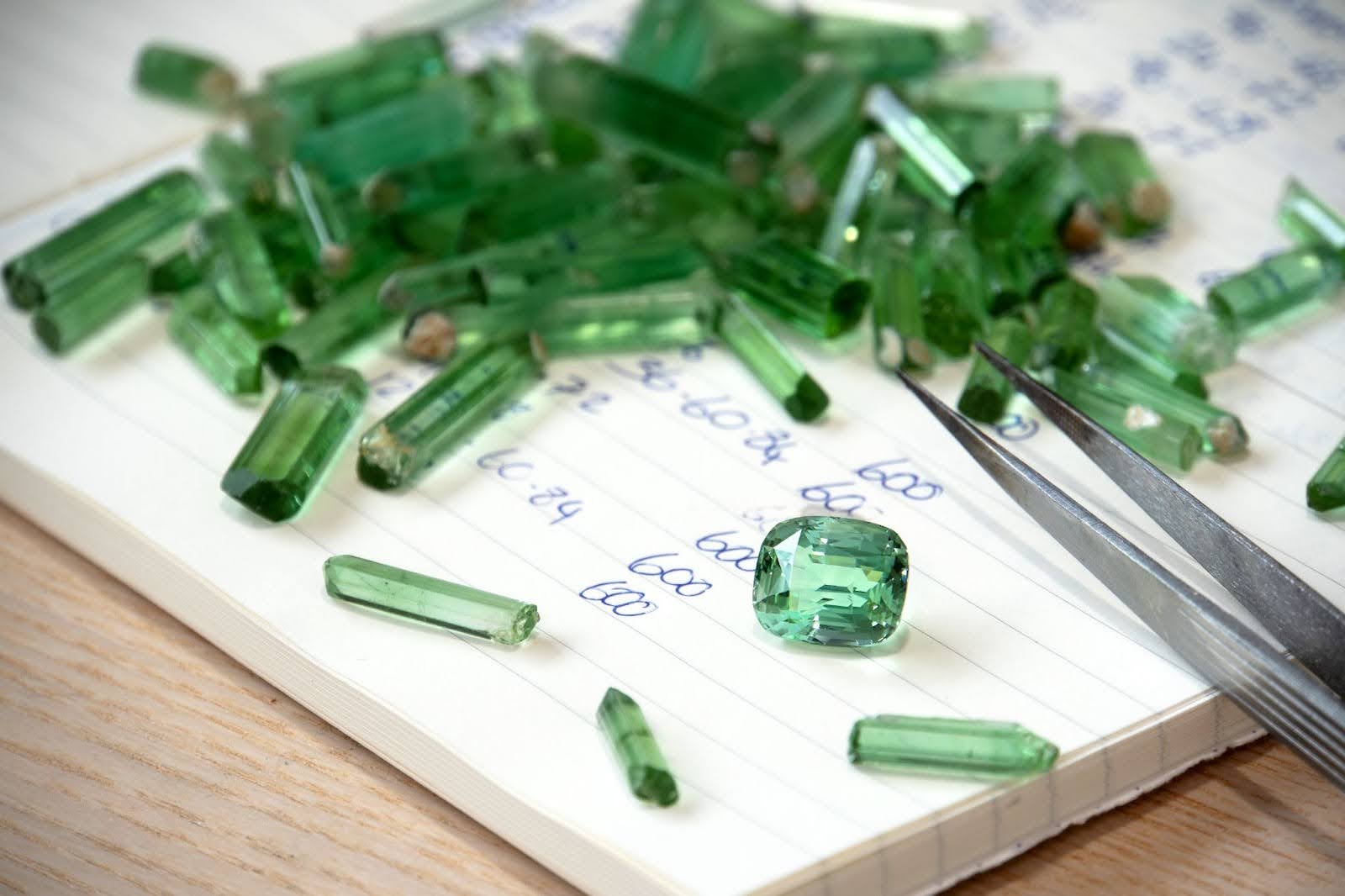  Green Tourmaline Roughs with a cut and polished Tourmaline Rectangle Cushion Gemstone on a notebook with Gemstone Tweezers at the corner