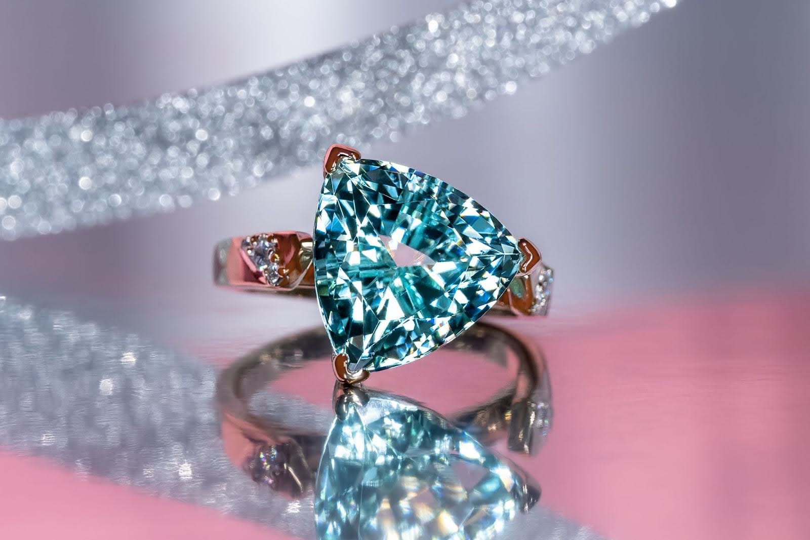 Close-Up of Sparkly Icy Light Blue Trillion Tourmaline Ring Studded with Diamonds along a Champagne Gold Band