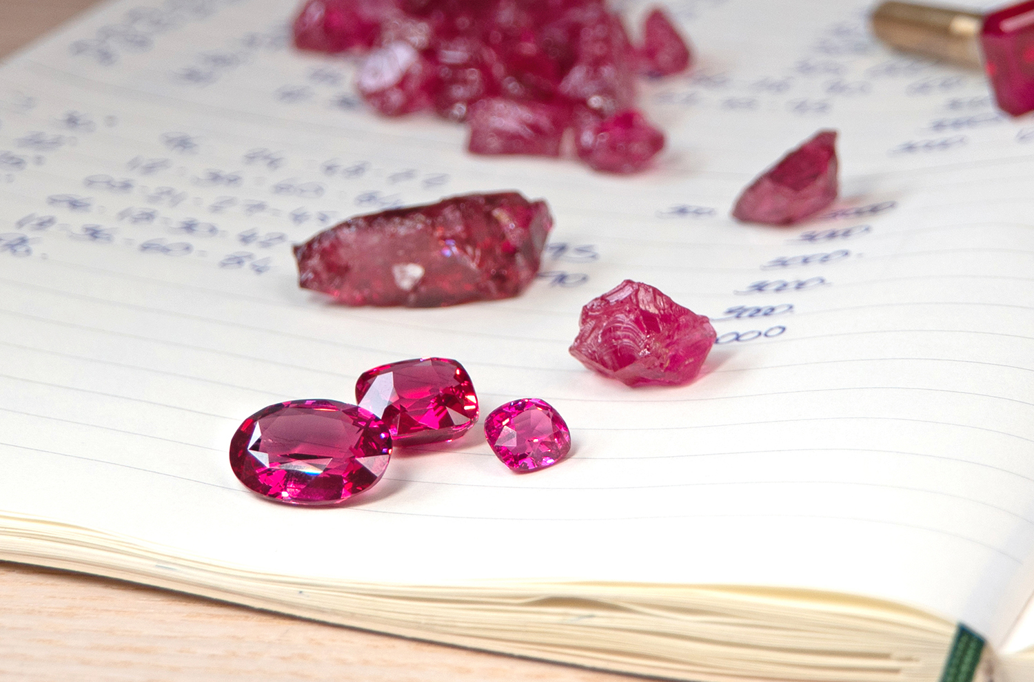 Mahenge Spinels in various gemstone cuts with their rough counterparts in the background.