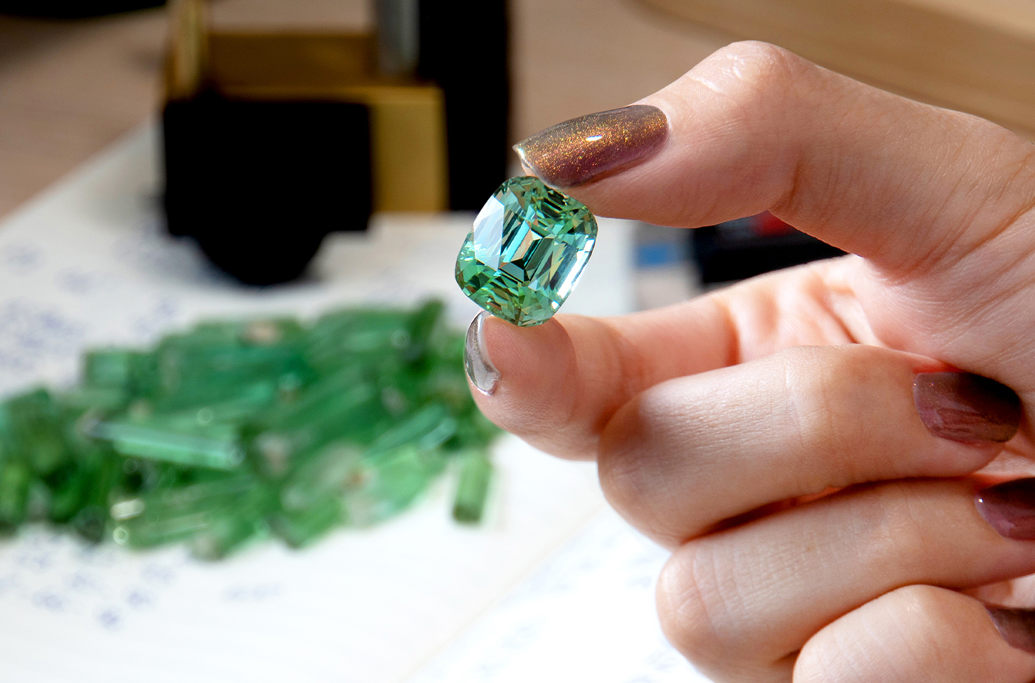 A cushion cut green Tourmaline against a pile of green Tourmaline roughs.